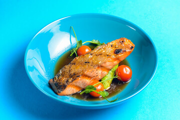 Fish steak with cherry tomatoes and soy sauce served in a blue bowl over blue background.
