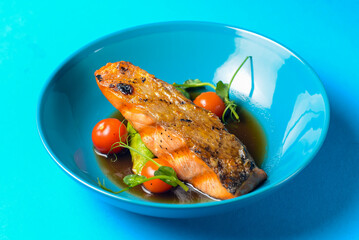 Fish steak with cherry tomatoes and soy sauce served in a blue bowl over blue background.