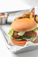Bacon burger with beef patty, fresh tomatoes and cucumbers with sauce served on a metal tray over white background.