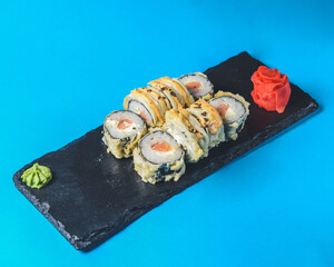 Japanese Sushi Roll - Warm Sushi Roll with Salmon and Cream Cheese served on a black board over bright blue background.