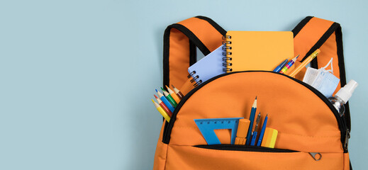 School background. Orange backpack with school supplies on a light blue background. Close-up, flat lay, horizontal, top view, copy space. Education concept.