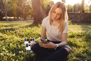 Girl skateboarder sits on the grass and using a smartphone