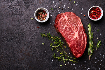 Fresh raw marbled beef rib eye steak and spices on black stone background, copy space - obrazy, fototapety, plakaty