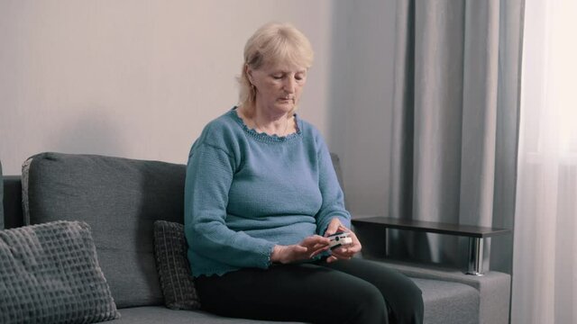 Elderly woman measures oxygen saturation. Pensioner uses pulse oximeter at home. Slider shot.