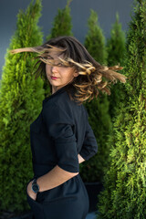 attractive fashionable woman in black dress posing near white cedar trees