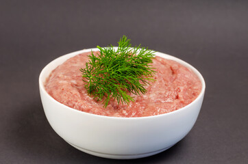 Raw ground meat and green dill on a gray background. White ceram
