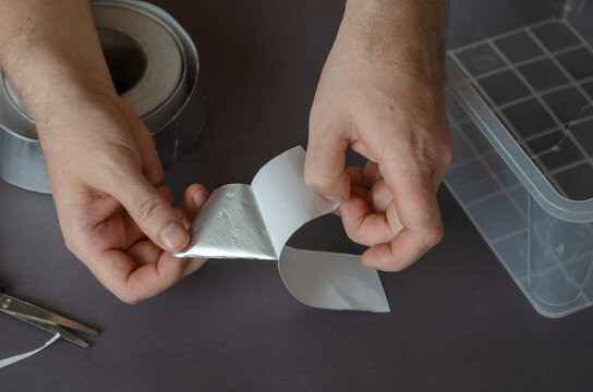 A man is peeling aluminum tape off the paper backing. The proces