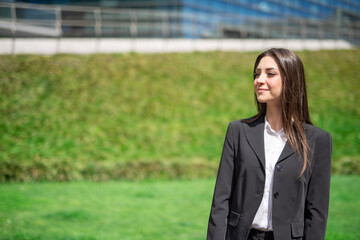 Smiling young woman near a grass field and a glass office building