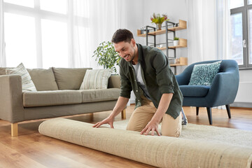 home improvement, interior and real estate concept - happy smiling young man unfolding carpet