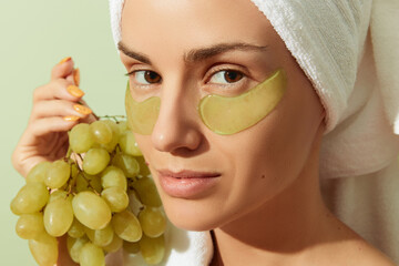 Woman using grapeseed-based eye patches on pastel green background. Natural sustainable skincare