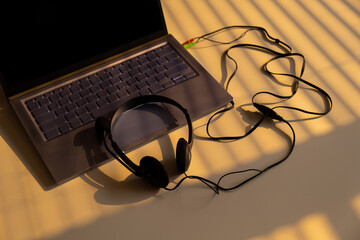 Headphones lie on a laptop keyboard on a white table. The shadow from the blinds falls on the desktop.