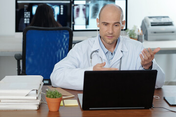 Fototapeta premium Doctor sitting at desk, having video call with colleague or patient and discussing disease treatment