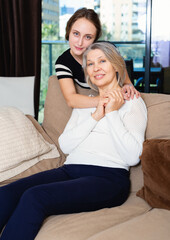 Portrait of loving adult daughter and elderly mother sitting on sofa at home