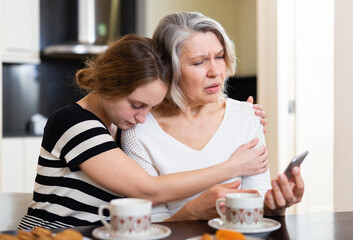 Sad young and elderly women looking at phone, having bad news