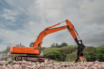 Red excavator with rock or stone grab attached to the arm. Heavy machinery equipment on a construction site