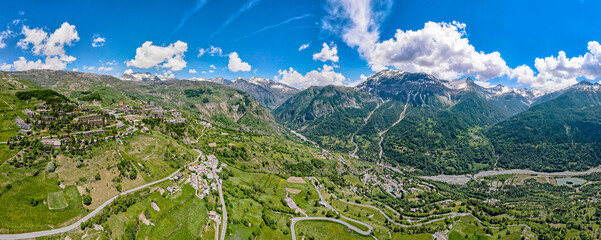Vibrant aerial panoramic of the Alps during springtime. Snow capped peaks, forest covered valley and glacier fed streams and waterfalls
