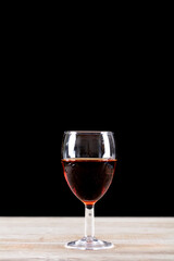 A glass of red wine on the table in front of black background