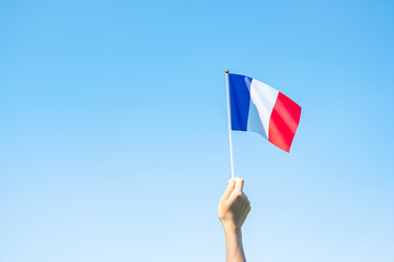hand holding France flag on blue sky background. holiday of French National Day, Bastille Day and happy celebration concepts