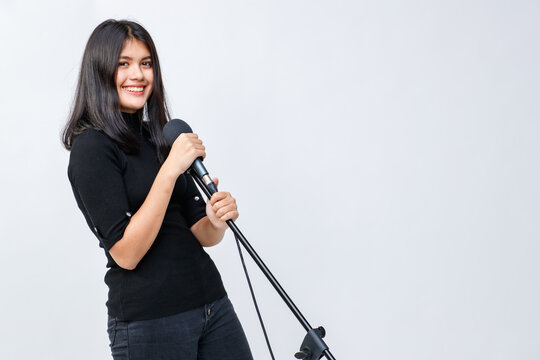 Portrait shot of an attractive smiling young Thai-Turkish teenager standing and holding the microphone while looking at the camera isolated in white background. There is copy space on side of image