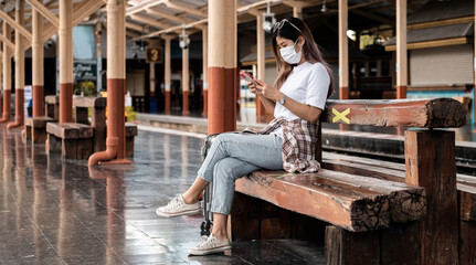 Asian tourist teenage girl wearing mask waiting distance train station using smartphone, social media check-in, lone traveler, Summer vacation railroad adventure concept.