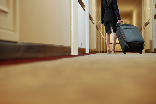 Woman with big suitcase walking down hotel corridor and looking for her room