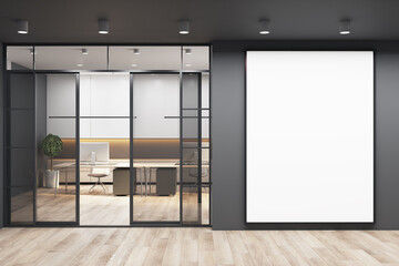 Blank white poster on black wall with copyspace for your logo next to doors to sunny office with monochrome style interior design, modern laptops on white tables and wooden floor. 3D rendering