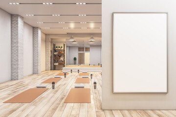 Modern concrete yoga gym interior with equipment, empty billboard on wall, daylight and wooden...