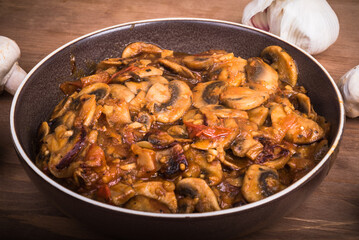 Mushroom stew in a plate. Fried mushrooms champignons with onions and tomatoes in a plate on a wooden table, close-up.