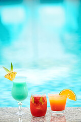 Various refreshing delicious cocktails decorated with fruit slices on edge of swimming pool of spa hotel