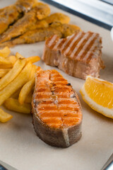 Grilled salmon steak with lemon and fries on light background.
