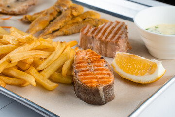 Grilled salmon steak with lemon and fries on light background.