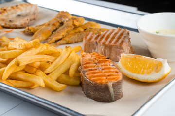 Grilled salmon steak with lemon and fries on light background.