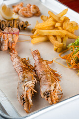 Set of seafood with large grilled shrimps on metal plate with carrot, lettuce close-up.
