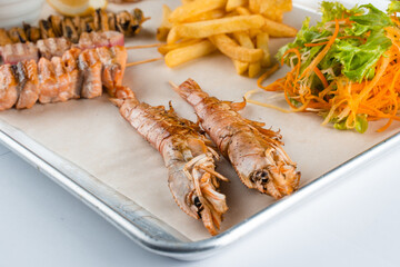 Set of seafood with large grilled shrimps on metal plate with carrot, lettuce close-up.
