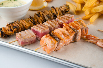 Barbecue seafood kebab with grilled mussels, tuna, salmon on a wooden skewer with white sauce and lemon.