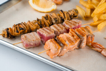 Barbecue seafood kebab with grilled mussels, tuna, salmon on a wooden skewer with white sauce and lemon.