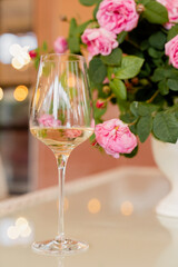 Glass of white wine against the background of bouquet roses in white vase on light table