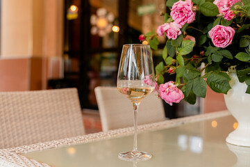 Glass of white wine against the background of bouquet roses in white vase on light table