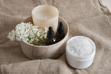 bath salt, white lilac, aroma candle and brown bottles with pipettes with aroma oil in a ceramic...