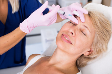 Obraz na płótnie Canvas Senior woman getting injection for facial rejuvenation procedure in esthetic clinic