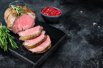 Roast beef fillet Tenderloin meat on a marble board. Black background. Top view. Copy space