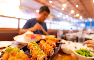 Selective focus on Japanese food in a Japanese restaurant. Salmon sushi on a plate with blurred man eating Japanese food with chopsticks in the restaurant. Healthy Asian food. Salmon sushi menu.
