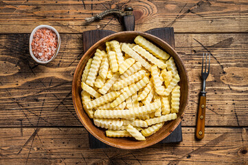 Cold Frozen Crinkle oven French fries potatoes sticks in a wooden plate. Wooden background. Top view