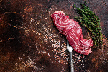 Raw machete skirt beef steak on meat fork. Dark background. Top view. Copy space