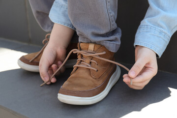 Little boy tying shoe laces on stairs outdoors, closeup