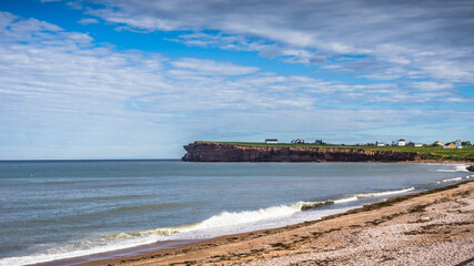 red sand beach and cliffs, blue sea, green grass, typical landscape of Gaspesie near Percé (Quebec, Canada)
