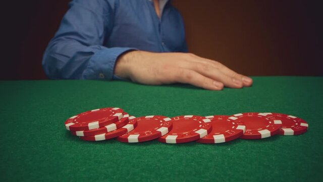 Male player moving casino chips on poker table close up