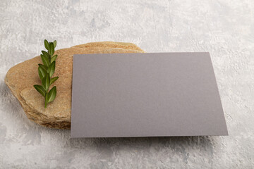 Gray paper business card, mockup with stone and boxwood branch on gray concrete background. side view, copy space.