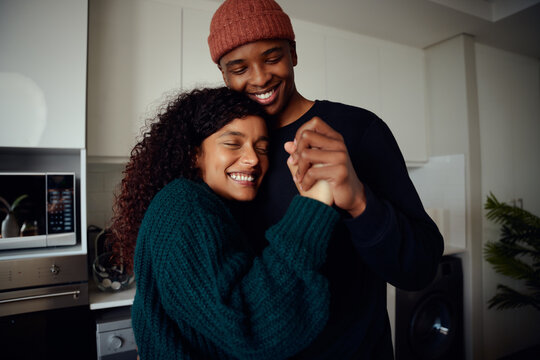 Young, happy mixed race couple holding hands in the kitchen. Mixed race couple dancing together and having fun. High quality photo