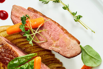Appetizing confit duck breast with pear and yellow apple puree, berry sauce in a white plate. Isolated on grey background.